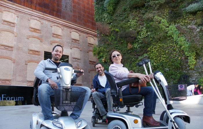 Three people posing sitting on their mobility scooter in front of the Caixa Forum in Madrid